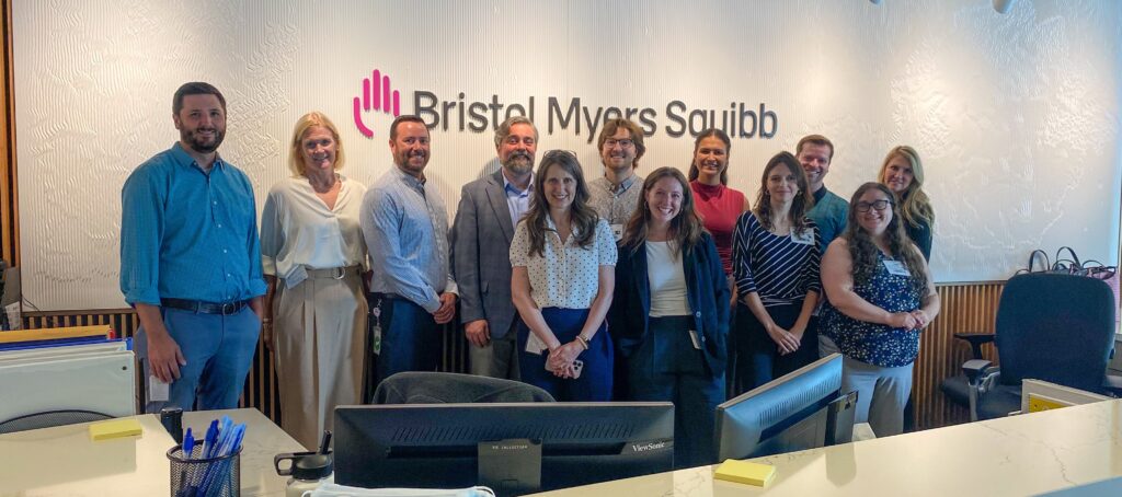 twelve smiling people standing in front of the Bristol Myers Squibb logo